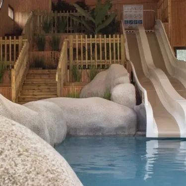 Piscine avec toboggan en bois et rochers décoratifs au Camping Le Palace