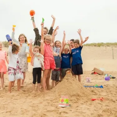 Enfants souriants devant une colline de sable avec jouets, à Camping Club Mahana