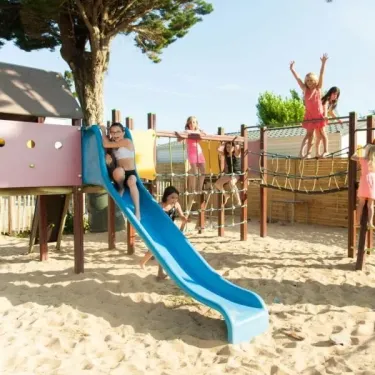 Enfants s'amusant sur une aire de jeu en bois avec toboggan bleu au Camping Club Mahana