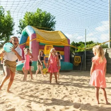 Enfants jouant au ballon sur sable près d'un manège gonflable à Camping Club Mahana
