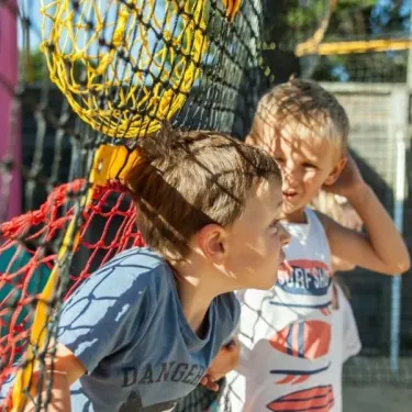 Enfants jouant près d'un filet jaune dans l'aire de jeux du Camping Club Mahana