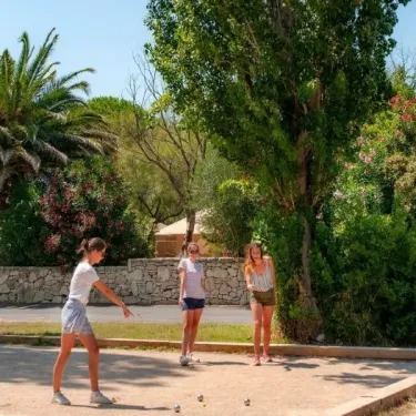 Trois jeunes femmes jouent au pétanque dans le jardin du Camping Ensoya, entourées d’arbres et de palmiers.