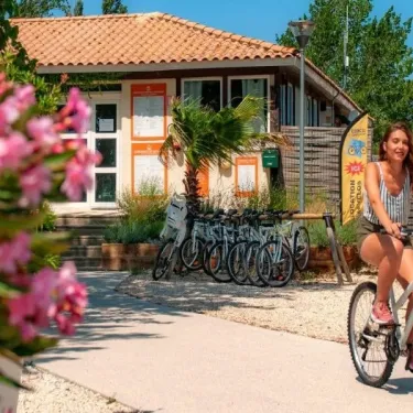 Femme à vélo près d'un kiosque du Camping Ensoya, avec des vélos alignés en arrière-plan.