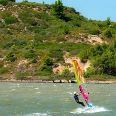 Personne windsurfant sur une mer agitée, près d'une côte végétée.