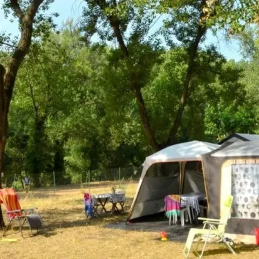 Camping La Plage de l'Orb : tente de camping dans une forêt, chaise pliante et table à l’extérieur.