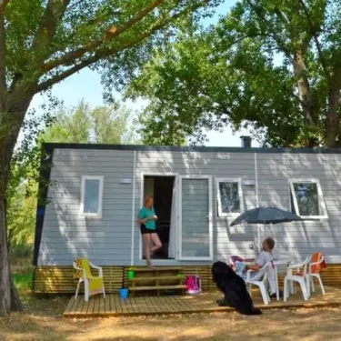 Mobile home gris au Camping La Plage de l'Orb, terrasse avec chaises et ombrelle.