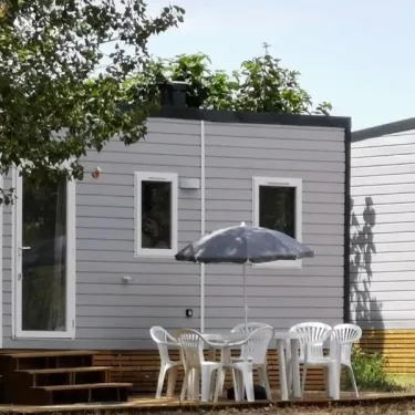 Camping La Plage de l'Orb : mobil-home gris avec table et chaises blanches sous un parasol.