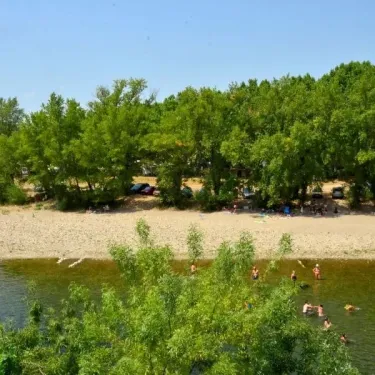 Camping La Plage de l'Orb : plage sablonneuse bordée d'arbres, visiteurs dans l'eau.