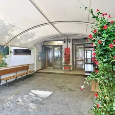 Entrée du camping avec banc en bois et plantes fleuries sous une structure en toile, Camping Le Parc des Chênes