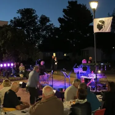 Camping Chanset : spectacle musical sur scène éclairée, public assis à table extérieure.