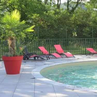Camping Chanset : piscine entourée de chaises longues rouges et d'une palme en pot.