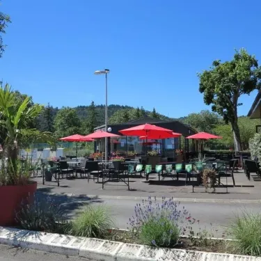 Terrasse avec parasols rouges et tables autour d'un bâtiment au Camping Chanset