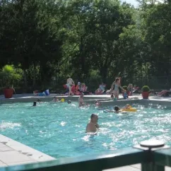 Camping Chanset : personnes qui nagent dans une piscine entourée d'arbres et de chaises longues.