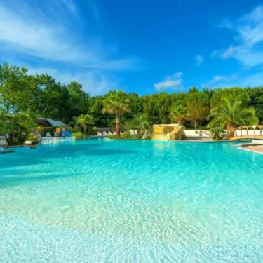 Piscine turquoise entourée d'arbres et de palmiers au Camping Aurilandes