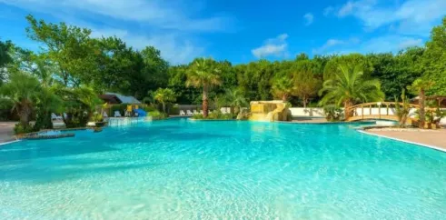 Piscine turquoise entourée d'arbres et de palmiers au Camping Aurilandes