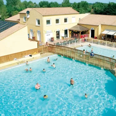 Camping Domaine les Fleurs d'Agde - piscine extérieure avec personnes nageant et bâtiment jaune à côté