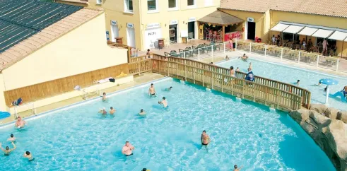Camping Domaine les Fleurs d'Agde - piscine extérieure avec personnes nageant et bâtiment jaune à côté