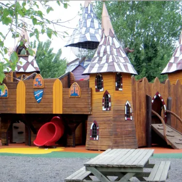 Parc d'attractions en bois avec château médiéval et toboggan rouge au Camping Domaine les Fleurs d'Agde