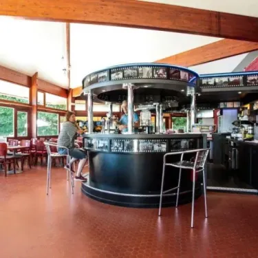 Intérieur d'un bar-restaurant avec comptoir circulaire et chaises rouges.