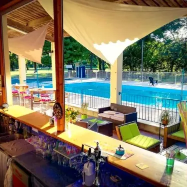 Bar extérieur du Camping Le Lion avec piscine en arrière-plan, canapés verts et plantes décoratives.