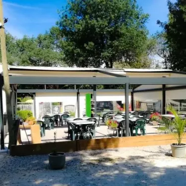 Camping Le Lion - terrasse ombrée avec tables et chaises vertes, plantes en pot, ciel bleu