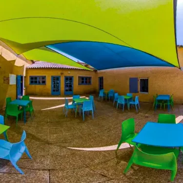 Courtyard avec tables et chaises colorées sous une bâche jaune et bleue, Camping Saint Maurice
