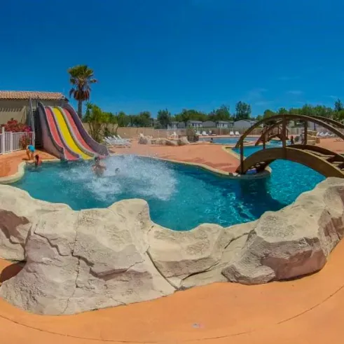 Piscine avec toboggan coloré et pont en bois au Camping Saint Maurice.