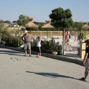 Jeux de boules dans la cour du Camping La Riviera avec des visiteurs autour.