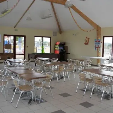 Salle à manger du Camping La Riviera avec tables et chaises, billard et jeux vidéo.