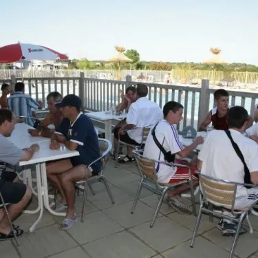 Terrasse du Camping La Riviera où des clients dégustent un repas sous une ombrelle.