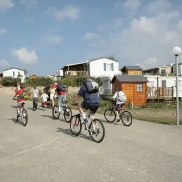 Camping La Riviera : enfants en vélo sur route avec mobil-homes en arrière-plan.