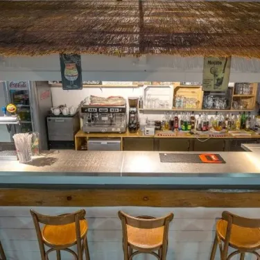 Camping L'Océan : bar avec toit en paille et tabourets en bois.