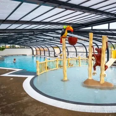 Zone ludique de la piscine avec mascotte toucan et singe, dans une structure couverte.