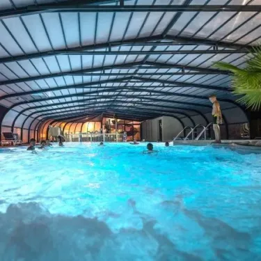 Piscine couverte avec eau turquoise, palmiers et enfants nageant à Camping L'Océan.