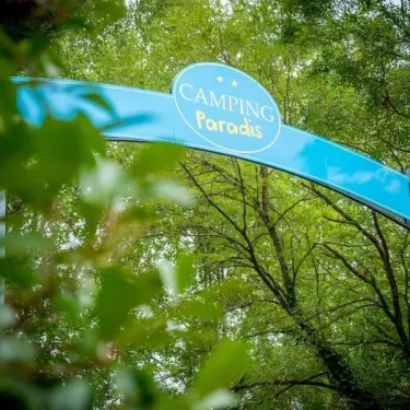 Entrée du camping Paradis avec arche bleue entourée de verdure