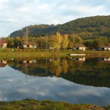 Camping du Lac de Moselotte : maisons en bord de lac avec reflets sur l'eau, montagne en arrière-plan.
