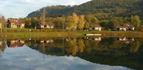 Camping du Lac de Moselotte : maisons en bord de lac avec reflets sur l'eau, montagne en arrière-plan.