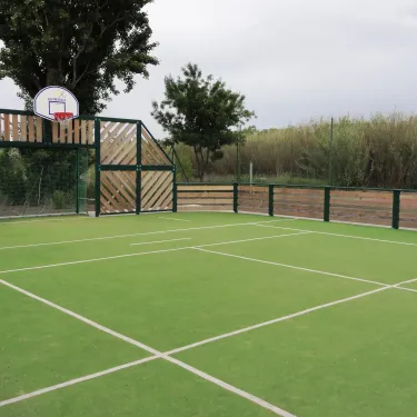 Court de basket-ball extérieur avec filet et clôture en bois au Camping Domaine les Fleurs d'Agde