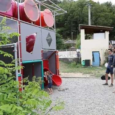 Camping Coeur d'Ardèche : enfants jouent sur une aire de jeux colorée avec des toboggans rouges.