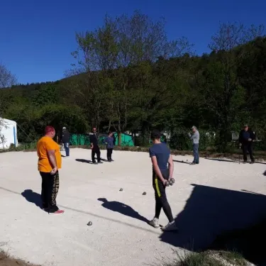 Camping Coeur d'Ardèche : groupe jouant au pétanque en plein air sous un ciel bleu.
