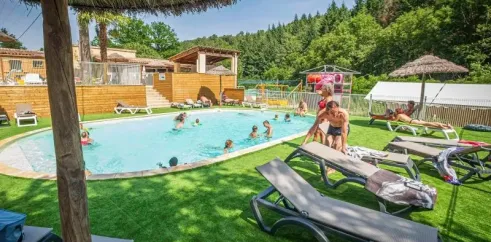 Piscine ovale du Camping Coeur d'Ardèche avec parasols en paille, chaises longues et enfants nageant.