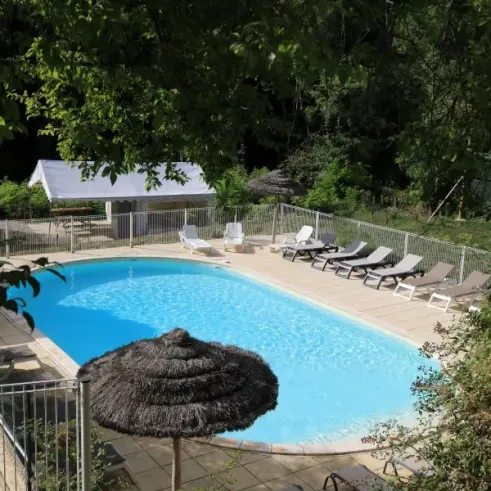 Piscine extérieure du Camping Coeur d'Ardèche entourée de chaises longues et d'ombrages naturels.