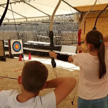 Enfants pratiquent l'archerie sous une tente à Camping Coeur d'Ardèche