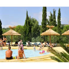 Piscine avec enfants et adultes au Camping Domaine des Naiades, sous parasols en paille.