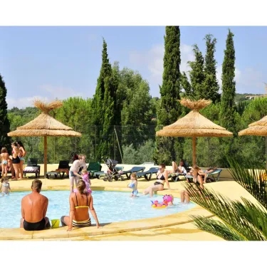 Piscine avec enfants et adultes au Camping Domaine des Naiades, sous parasols en paille.