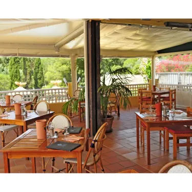 Terrasse de restaurant avec tables en bois et chaises, sous une toile de protection.