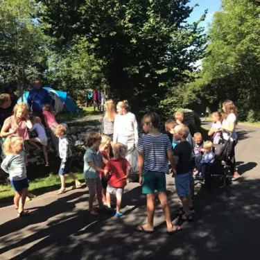 Enfants et adultes au Camping Le Clos de Banes, près d'une tente bleue sous des arbres