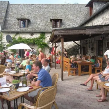 Groupes de personnes dégustant un repas à l'extérieur du Camping Le Clos de Banes, dans une cour pavée