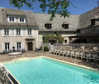 Piscine et piscine en plein air au Camping Le Clos de Banes, entourée d'une maison traditionnelle.