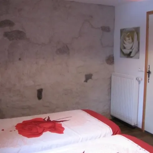 Chambre Quadruple - Le Clos de Banes : chambre avec deux lits et mur texturé.
